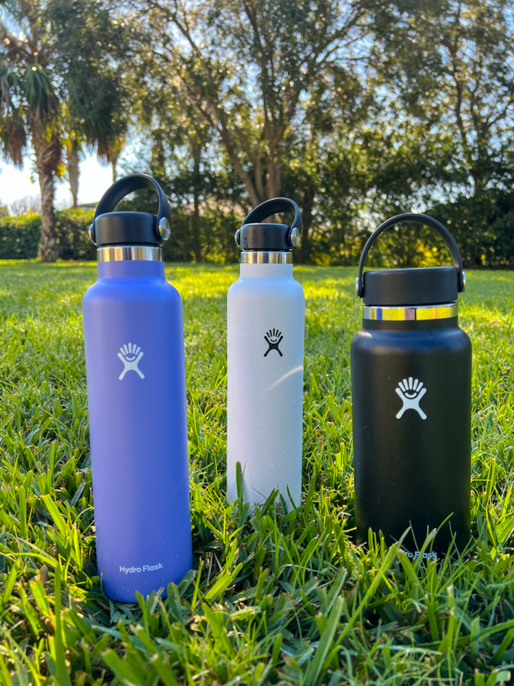 All different size and color Hydro Flask water bottles set in a grassy background