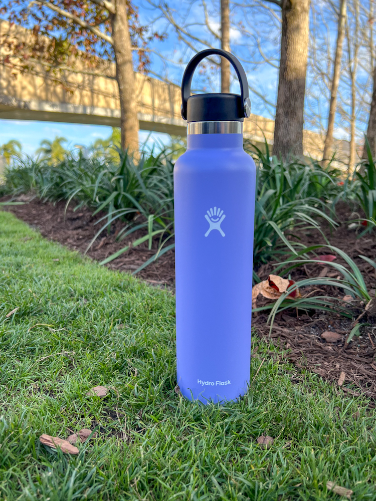 Purple Hydro Flask water bottle set in a grassy background