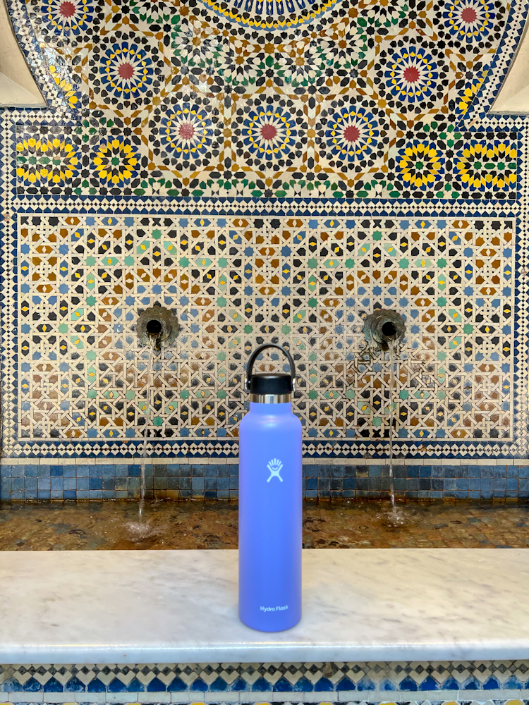 Purple hydro flask water bottle set in front of a Moroccan water feature