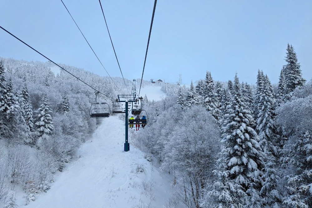 A view of the ski lift above the snowy trees and snowy ski area of Mont Tremblant, Canada