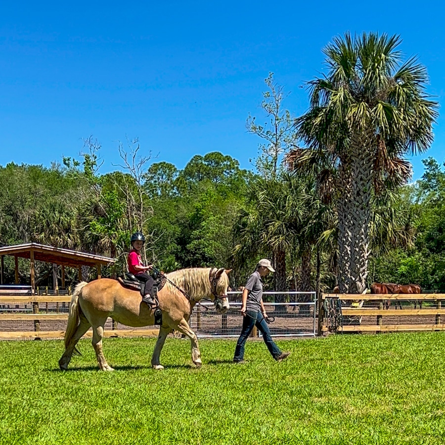 kid riding a horse being led by a trainer at Hidden Palms Ranch in Sanford, Florida