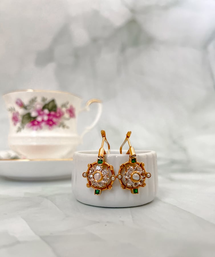 vintage earring with emeralds, pearls, and cz hanging from a jewelry box with a vintage teacup and saucer in the background