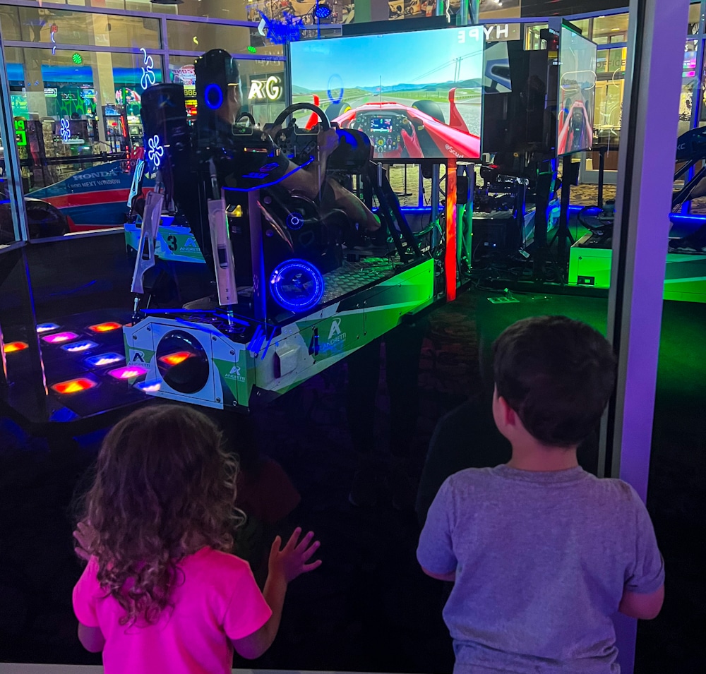 toddler brother and sister watching dad play a simulator car game