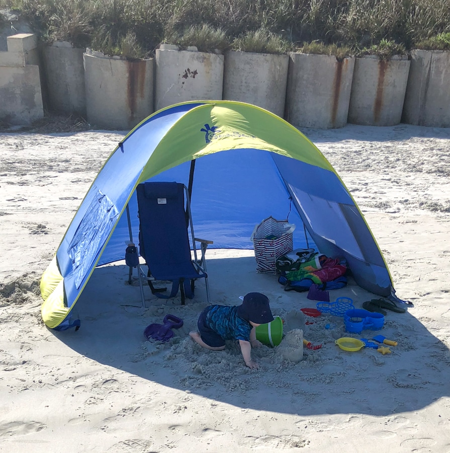 baby playing in the sand underneath the shade of a beach sun canopy