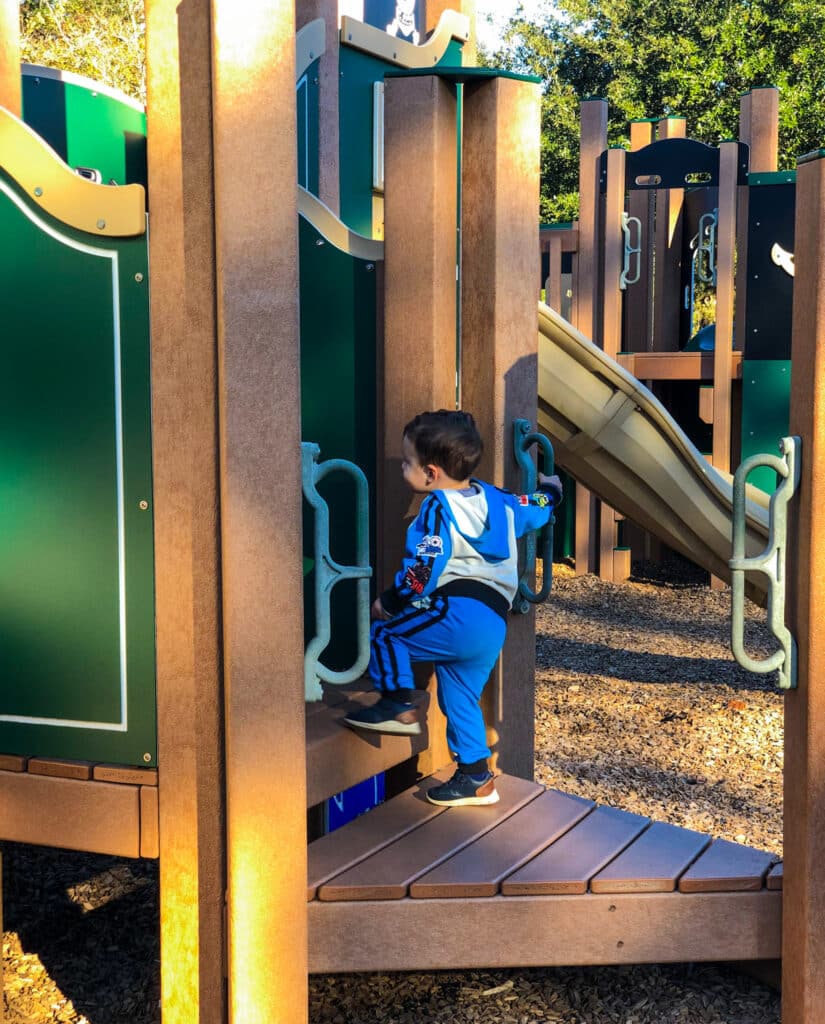 toddler boy climbing on a playground structure